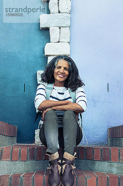 Porträt einer lächelnden  selbstbewussten Frau  die auf einer Backsteintreppe sitzt