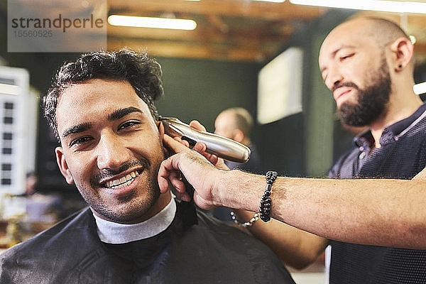 Porträt eines lächelnden jungen Mannes  der beim Friseur einen Haarschnitt erhält