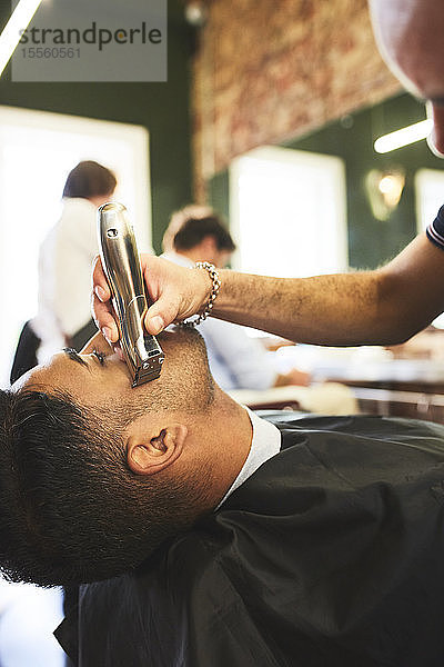 Männlicher Friseur rasiert das Gesicht eines Kunden im Friseursalon