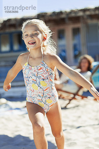 Unbekümmertes Mädchen im Badeanzug läuft am sonnigen Strand