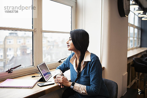 Nachdenkliche Geschäftsfrau bei der Arbeit am digitalen Tablet im Bürofenster
