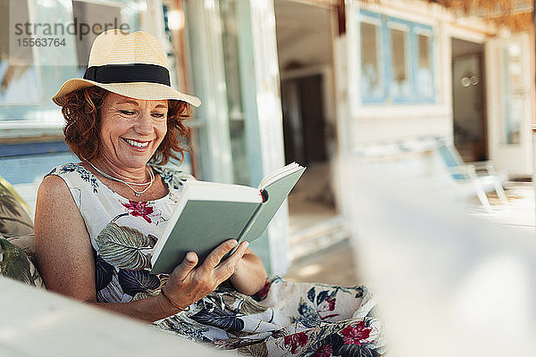 Glückliche Frau  die auf der Terrasse einer Strandhütte ein Buch liest