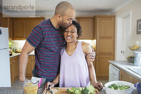 Zärtlicher Ehemann umarmt Frau beim Kochen in der Küche