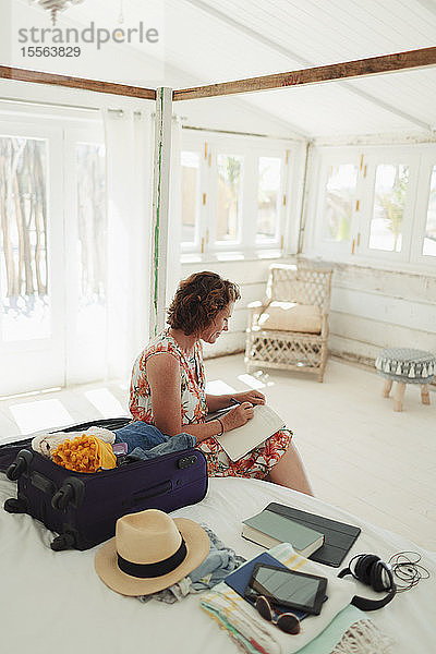 Frau schreibt in Tagebuch neben Koffer im Schlafzimmer einer Strandhütte