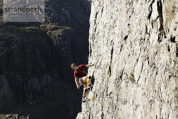 Männlicher Bergsteiger  der eine große Felswand erklimmt und über die Schulter nach unten schaut