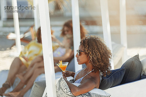 Junge Frau entspannt sich mit einem Cocktail auf einer Strandterrasse