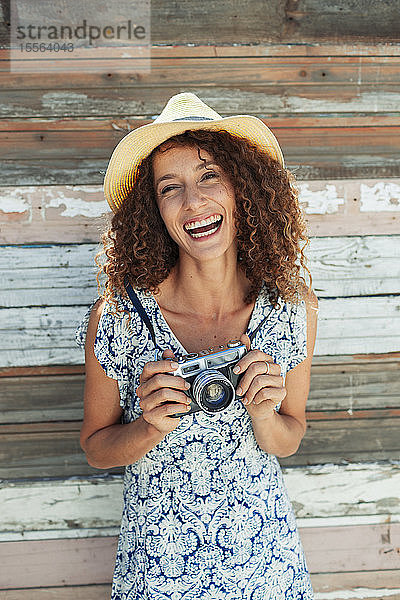 Porträt einer glücklichen  sorglosen jungen Frau mit Retro-Kamera vor einer Wand aus Holzplanken