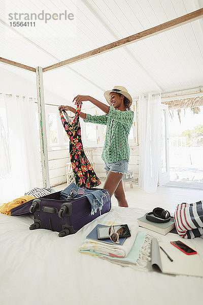 Glückliche Frau beim Auspacken des Koffers im Schlafzimmer des Strandhauses