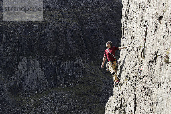 Männlicher Bergsteiger  der eine hohe Felswand erklimmt und über die Schulter blickt