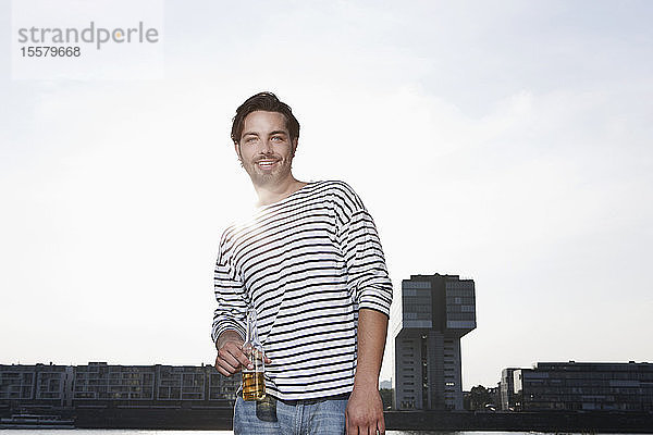 Deutschland  Köln  Junger Mann mit Bierflasche  lächelnd  Porträt