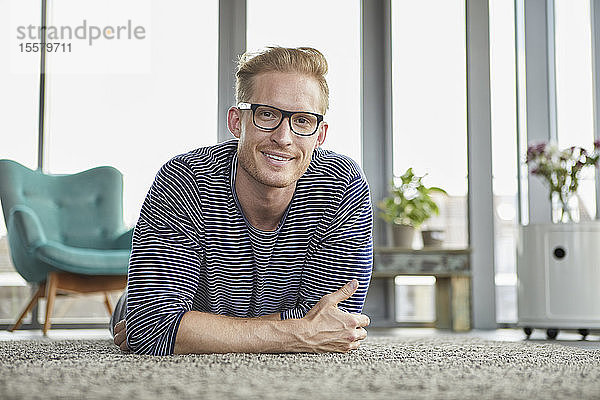 Porträt eines lächelnden jungen Mannes  der zu Hause auf einem Teppich liegt