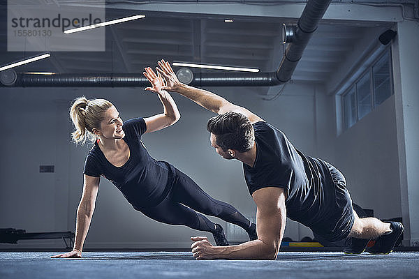 Mann und Frau machen High-Five während der Seitenplanken-Übung im Fitnessstudio