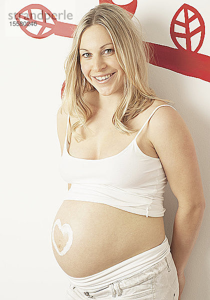 Schwangere Frau mit cremefarbenem Herz auf dem Bauch  lächelnd  Porträt