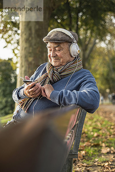 Älterer Mann auf Parkbank mit Handy und Kopfhörern