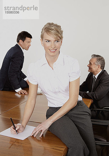 Frau im Büro sitzt am Schreibtisch  während im Hintergrund ein Geschäftsmann sitzt