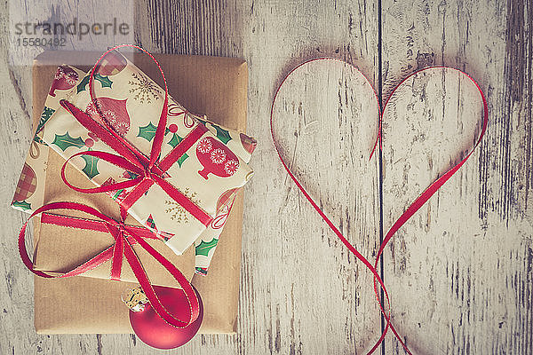 Stapel Weihnachtsgeschenke  rote Weihnachtskugel und Band in Herzform auf Holz