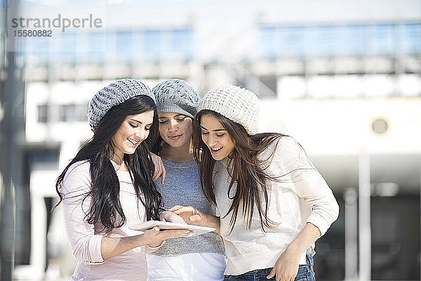 Drei Freundinnen mit Wollmützen mit digitalem Tablett
