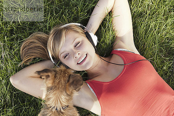 Deutschland  Köln  Junge Frau mit Hund im Gras liegend  lächelnd