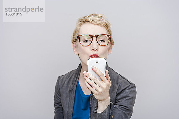 Blonde Frau mit Schmollmund  die sich mit ihrem Smartphone ein Selfie nimmt