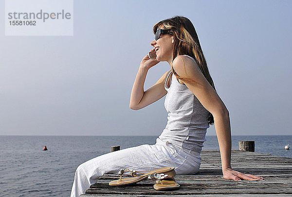 Italien  Gardasee  Womann 20-25) auf der Kante des Docks sitzend mit Mobiltelefon  Seitenansicht