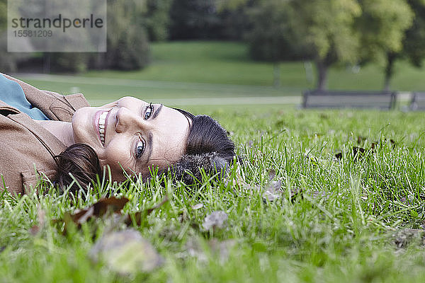 Deutschland  Köln  Junge Frau im Gras im Park liegend  lächelnd  Porträt