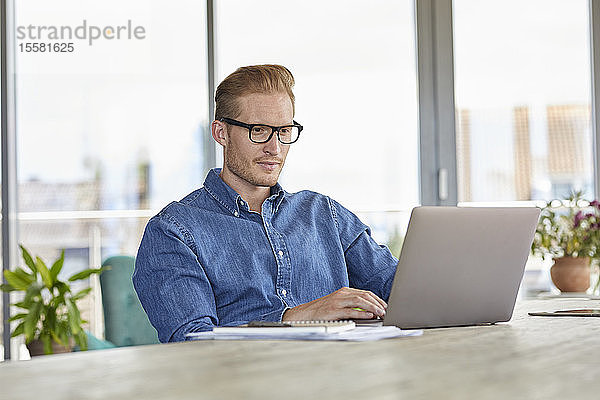 Junger Mann sitzt mit Laptop am Tisch