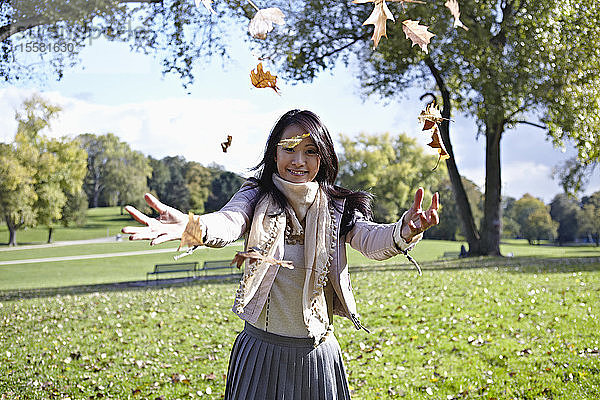 Deutschland  Köln  Junge Frau spielt im Park mit Blättern  lächelnd  Porträt