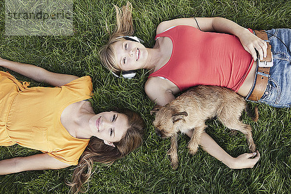 Deutschland  Köln  Junge Frau im Gras liegend mit Hund  lächelnd  Porträt