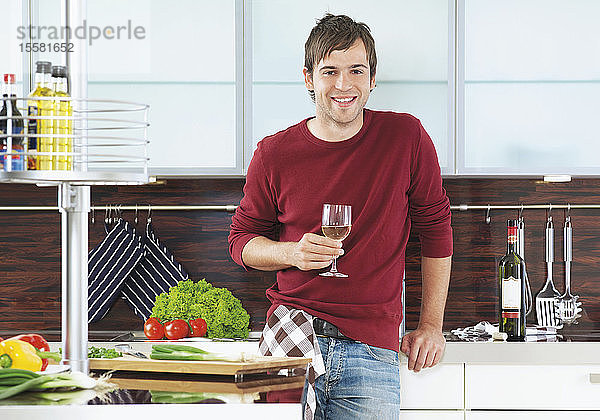 Deutschland  Junger Mann mit Weinglas in der Küche