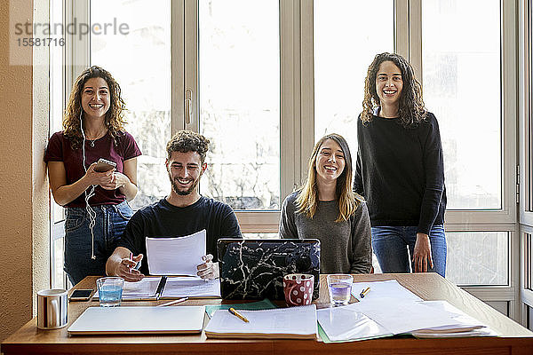 Porträt von vier glücklichen Studenten am Schreibtisch und am Fenster