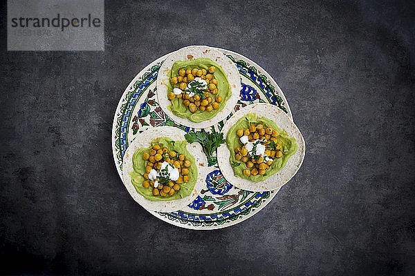 Fladenbrot mit Avocadocreme und Kurkuma-Kichererbsen im Teller auf dem Tisch