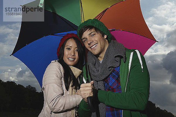 Deutschland  Köln  Junges Paar mit Regenschirm im Park  lächelnd  Porträt
