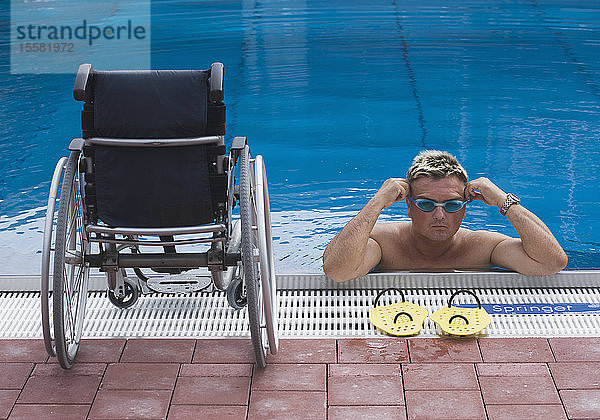 Deutschland  Ingolstadt  Behinderter Mann im Schwimmbad und Rollstuhl am Rande