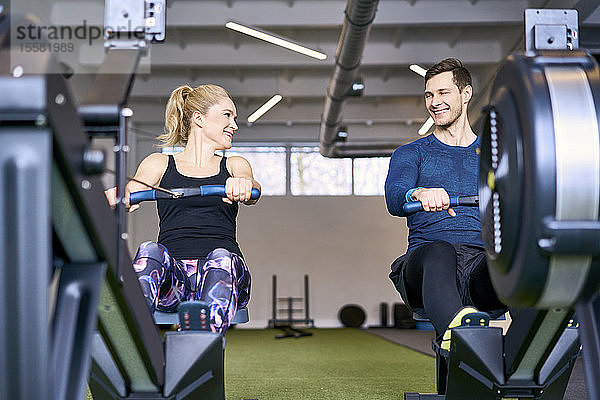 Mann und Frau im Fitnessstudio üben gemeinsam an Rudergeräten