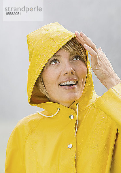 Frau im gelben Regenmantel schaut auf und lächelt