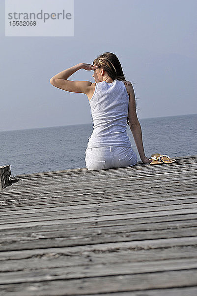 Italien  Gardasee  Junge Frau (20-25) auf dem Dock sitzend  Rückansicht  Nahaufnahme