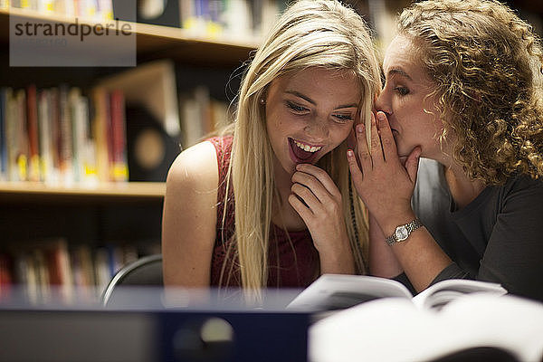 Zwei Studentinnen tuscheln in einer Bibliothek