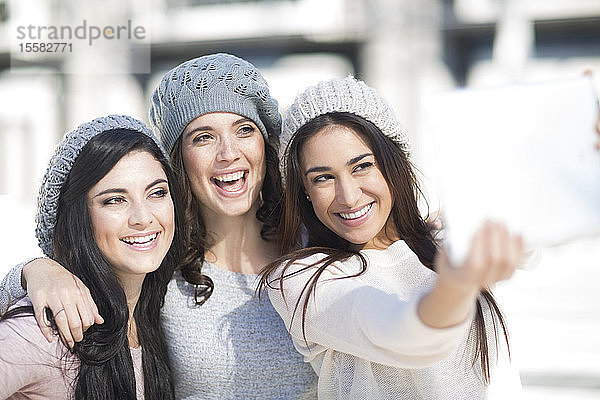 Drei Freundinnen mit Wollmützen bei einem Selfie mit digitalem Tablett