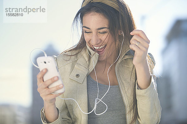 Porträt einer lachenden Frau mit Smartphone und Kopfhörern beim Musikhören