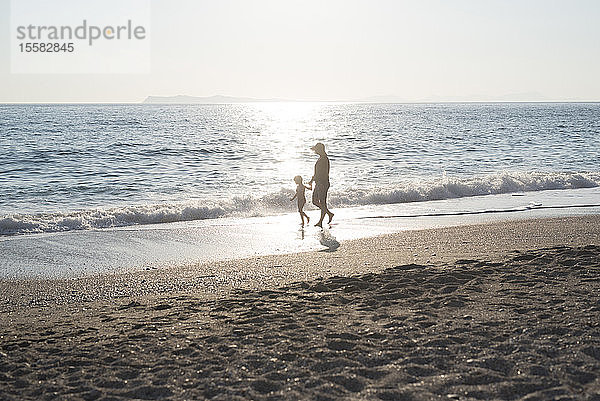 Griechenland  Parga  Mutter und Tochter gehen bei Sonnenuntergang am Strand spazieren