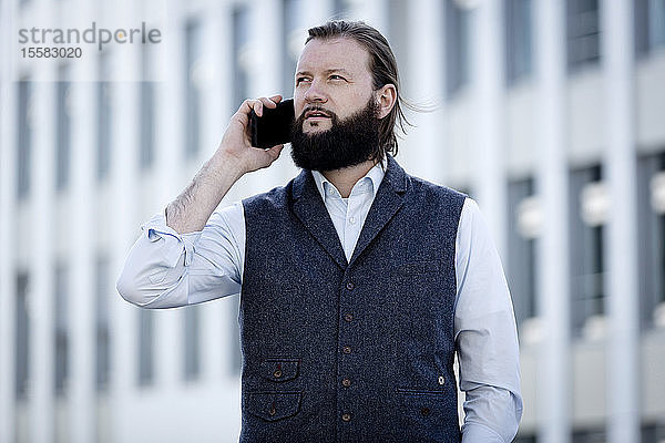Porträt eines bärtigen Geschäftsmannes mit Weste am Telefon