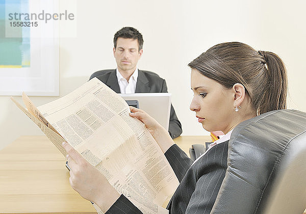 Geschäftsmann arbeitet am Laptop und Frau liest Zeitung im Büro