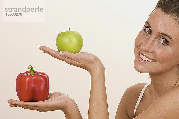 Junge Frau hält Apfel und Paprika  lächelnd  Porträt