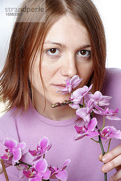 Junge Frau riecht Orchidee  Porträt  Nahaufnahme