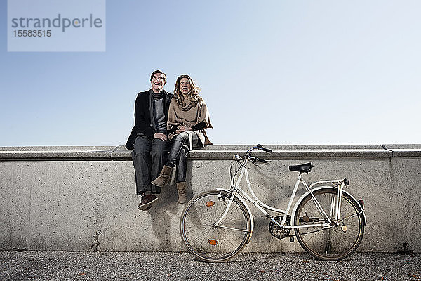 Deutschland  Bayern  München  Junges Paar mit Fahrrad an der Wand sitzend