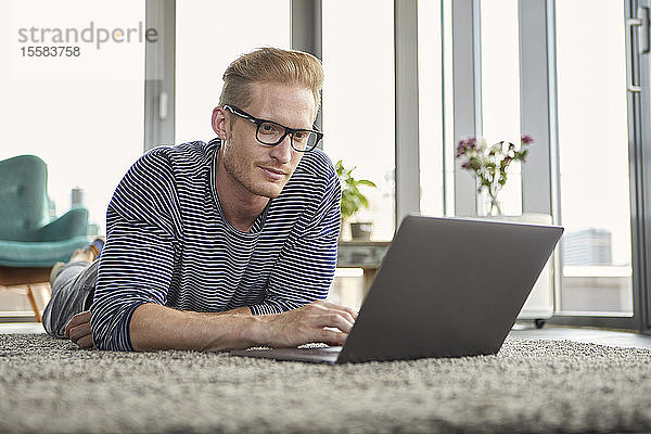 Junger Mann liegt zu Hause mit Laptop auf Teppich