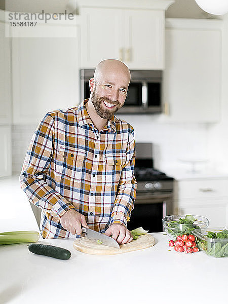 Lächelnder Mann hackt Gemüse in der Küche