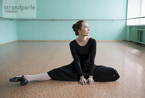 Balletttänzerin im schwarzen Kleid beim Stretching im Studio