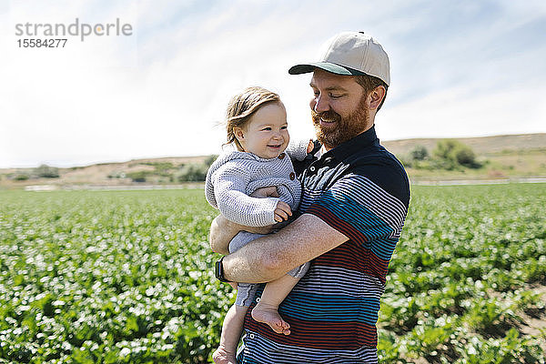 Lächelnder Vater hält kleines Mädchen in einem Getreidefeld