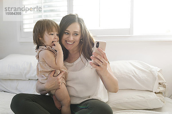 Mutter und Tochter machen ein Selfie auf dem Bett